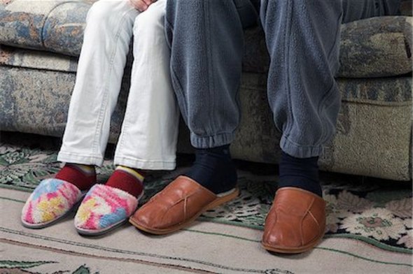 Close-up of a couple sitting on a couch with their leg/foot touching from the knees down.
